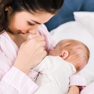 portrait of young mother breastfeeding little baby on bed at home